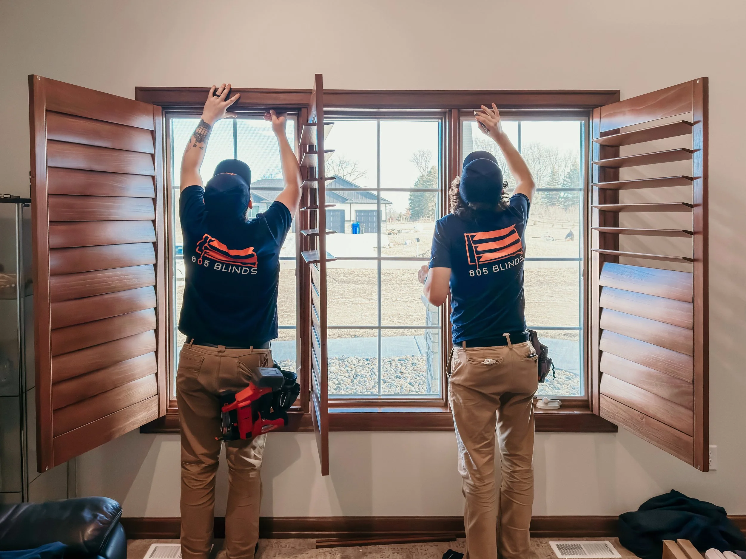 Two 605 Blinds Install Techs hanging wood plantation shutters in a bedroom window